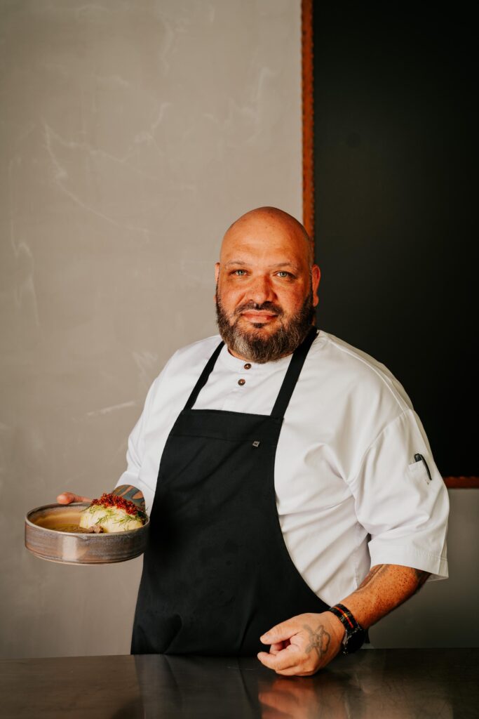 a man wearing a black apron holding a plate of food